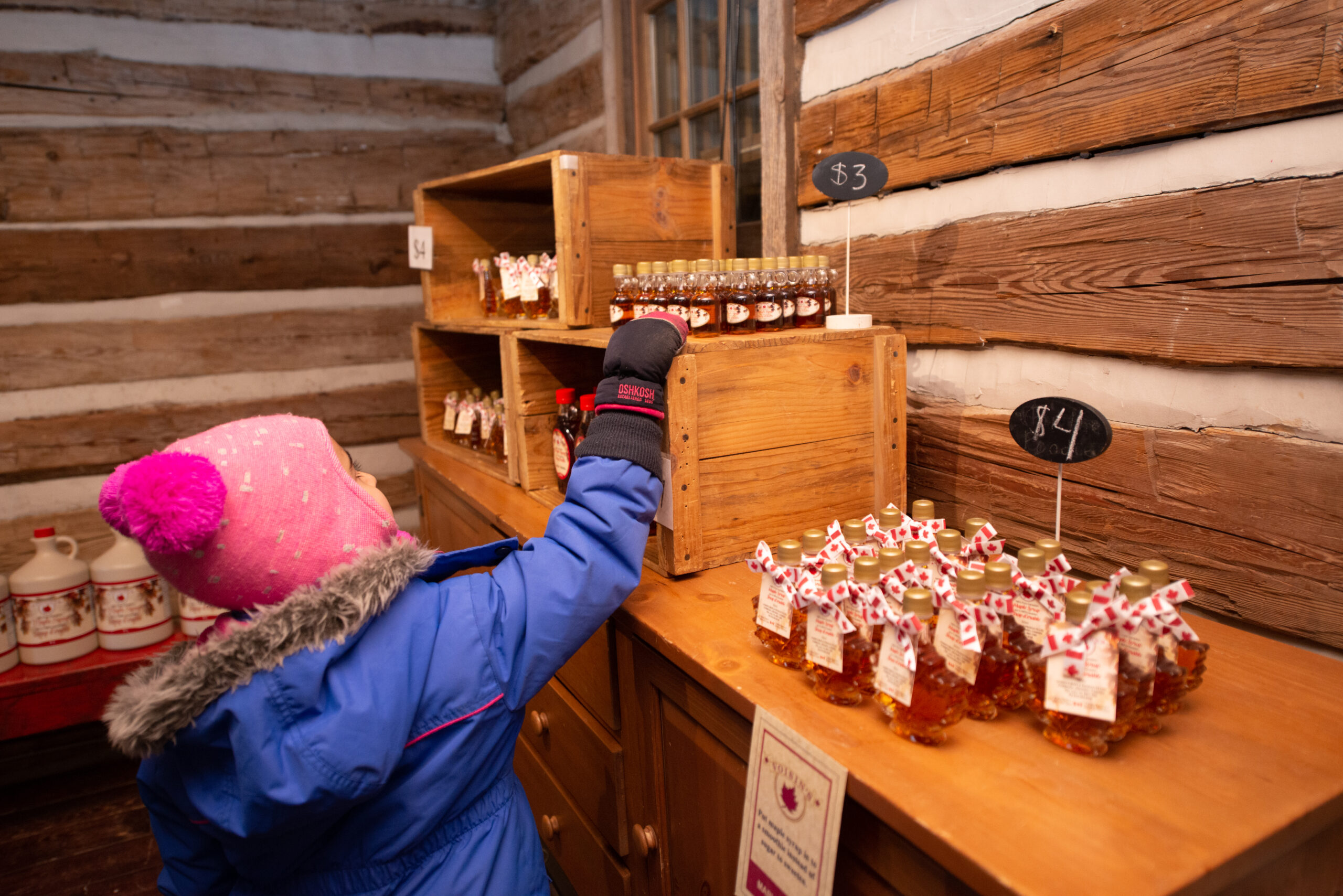 A child reaching for maple syrup on a shelf.